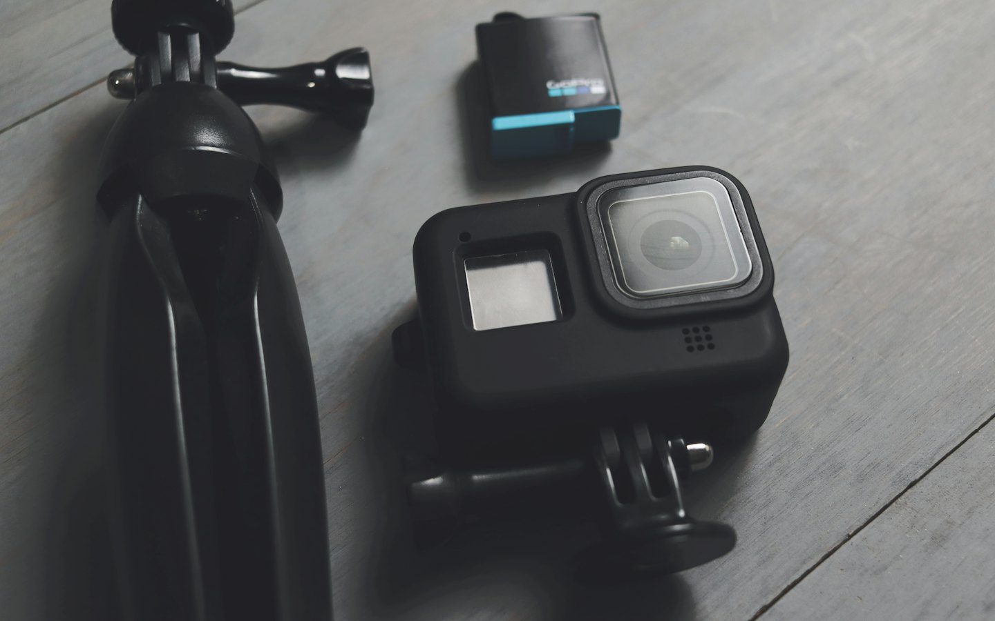 Action camera, tripod, and spare battery on a wooden surface.