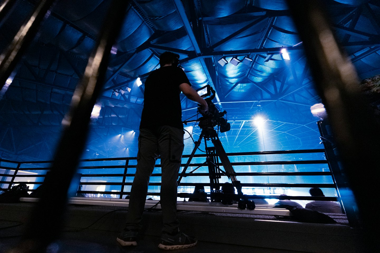Videographer operates a camera on a tripod at a stage event.